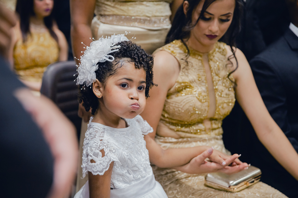 Daminha com tiara linda de flor na cabeça fazendo biquinho durante casamento em igreja evangélica em Pádua. RJ