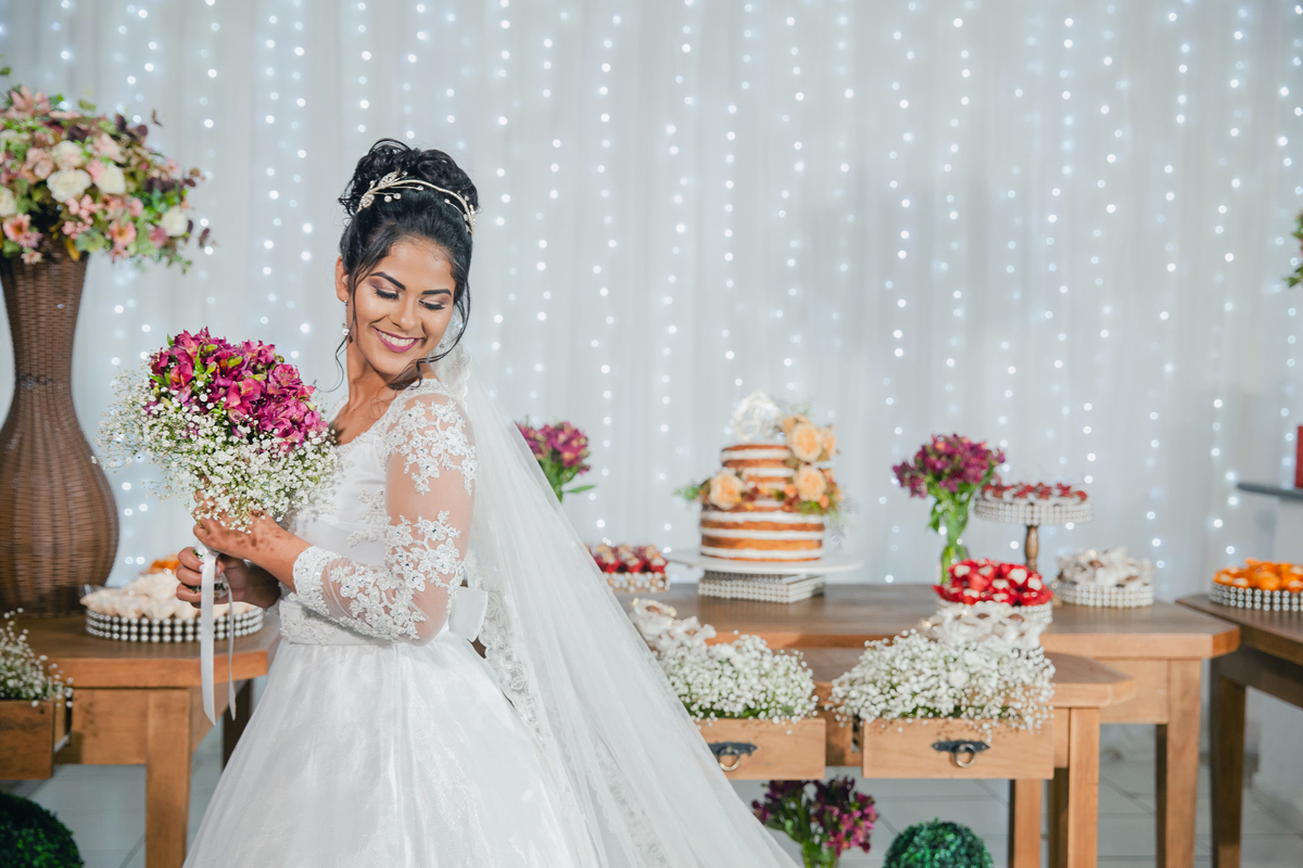 Noiva sorrindo olhando para baixo com penteado na cabeça e tiara de cristais com buque de flores rosa durante a festa de casamento em Santo Antônio de Pádua no rio de Janeiro.