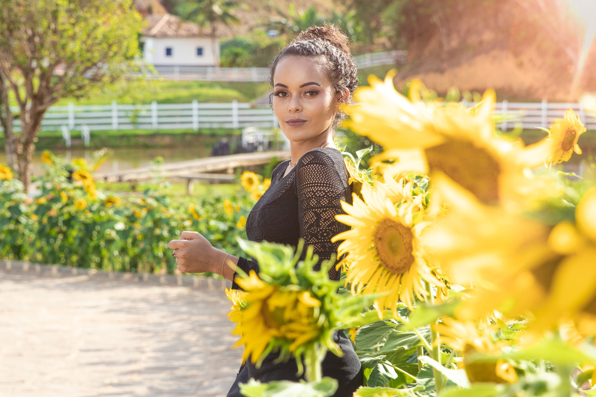 Menina de 15 anos com vestido preto e justo ao lado de girassóis posando para seu ensaio em Santo Antônio de Pádua no interior do Rio de Janeiro.