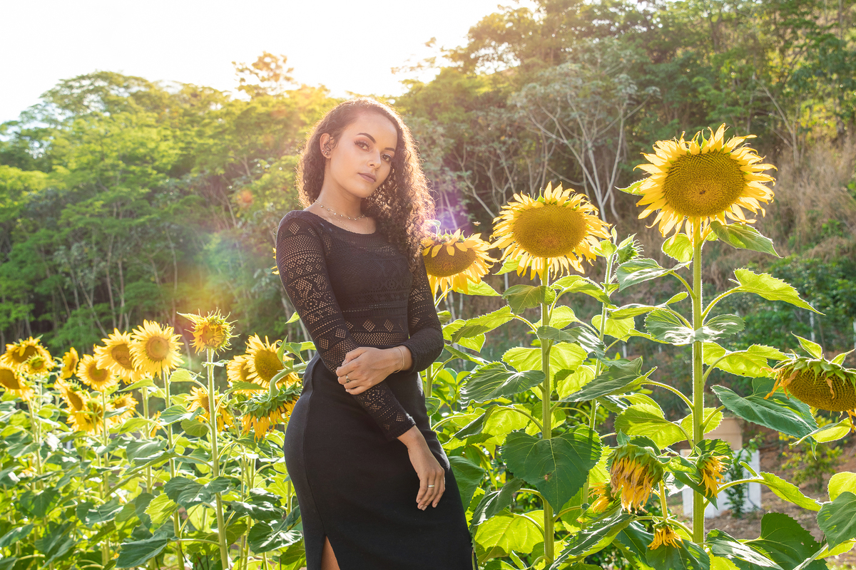 Debutante de 15 anos com vestido preto e justo ao lado de girassóis posando para seu ensaio  em uma fazenda antiga em Santo Antônio de Pádua no interior do Rio de Janeiro.