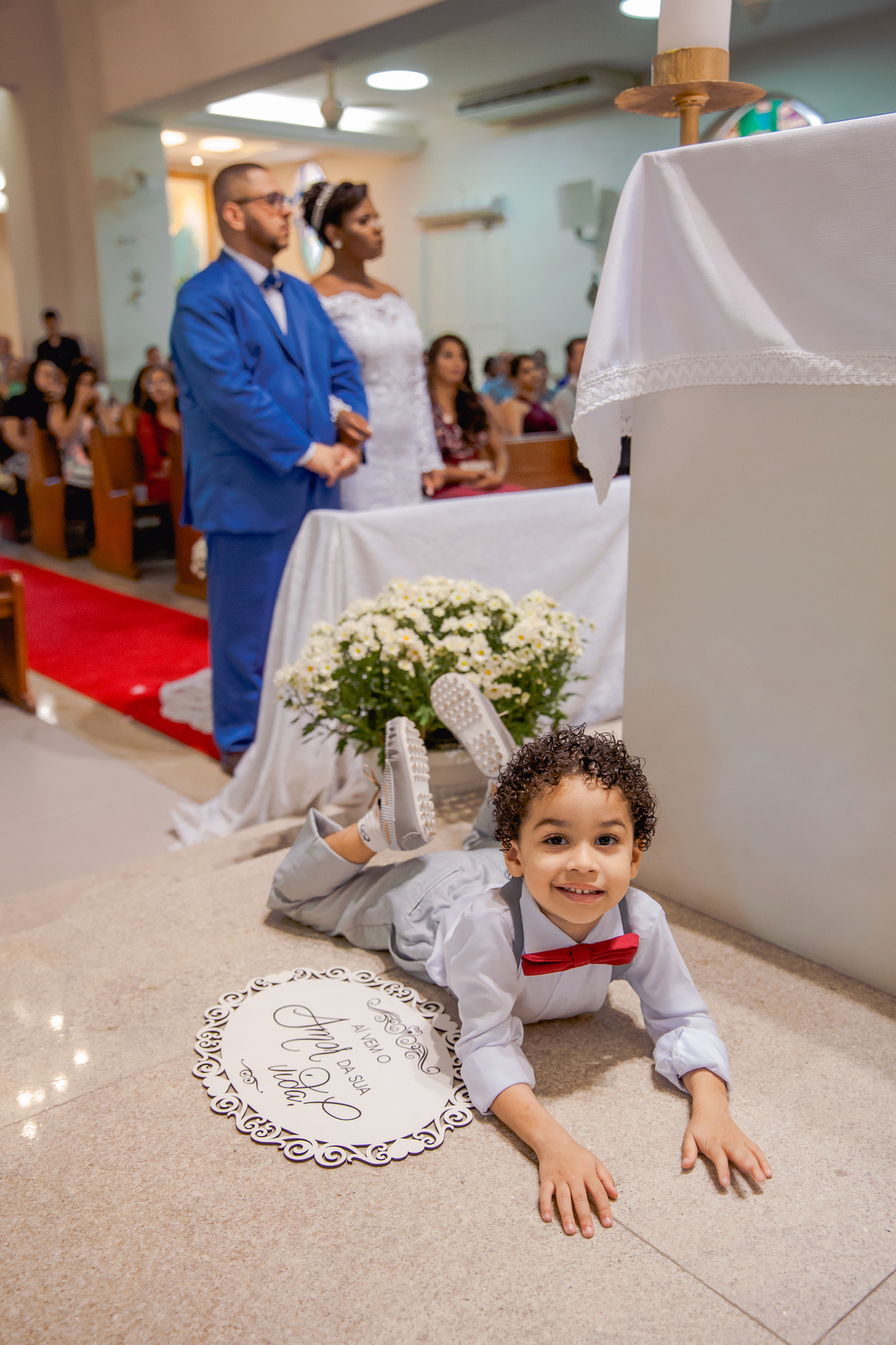 Pagem deitado no chão de pernas para cima brincando durante cerimônia de casamento na Paróquia de São José  de Leonissa em Itaocara no Rio de Janeiro.