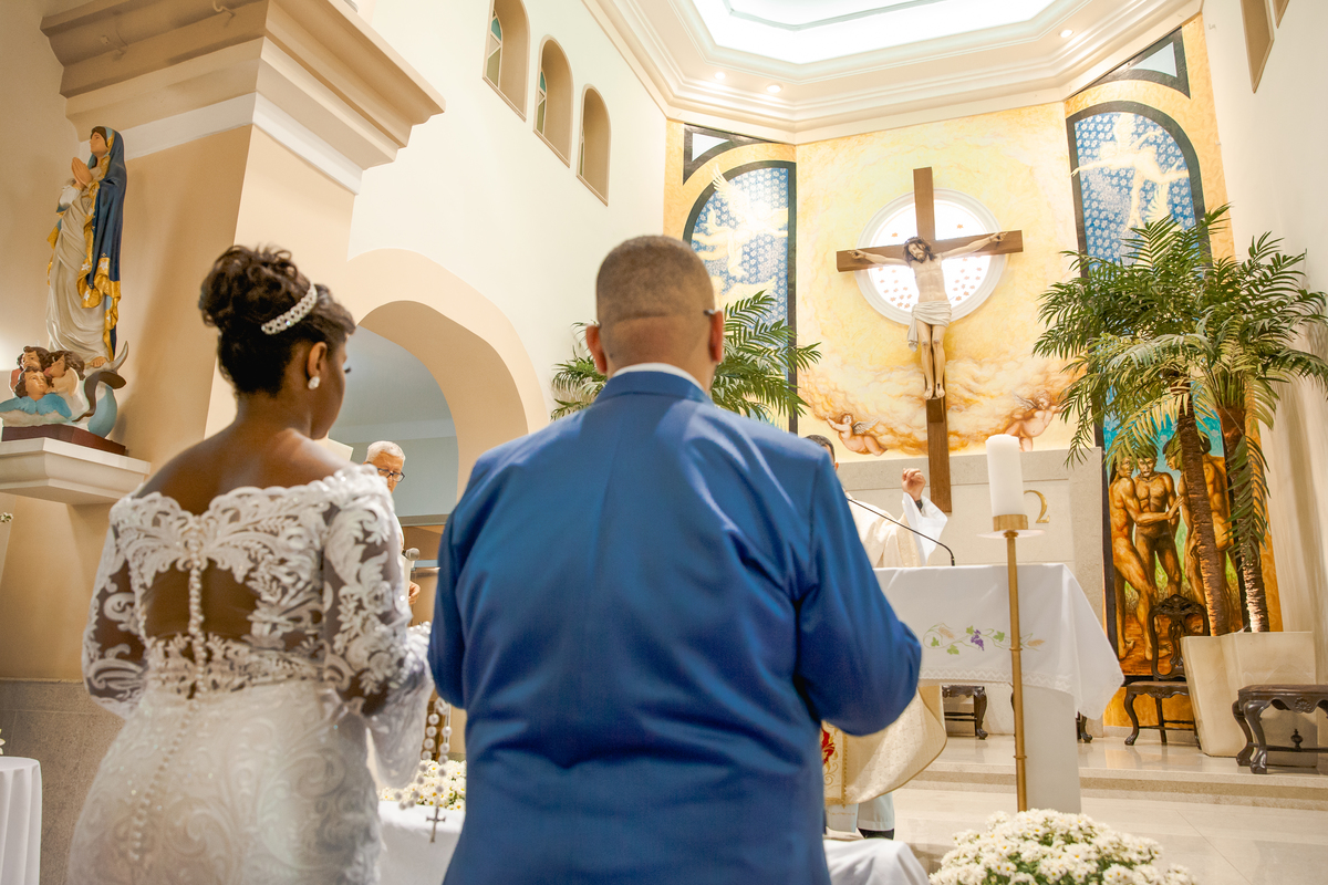 Noivos emocionados recebendo a benção durante cerimônia de casamento na Paróquia de São José de Leonissa em Itaocara no Rio de Janeiro. Noiva de vestido de renda lindo e noivo de terno azul de gravata borboleta.