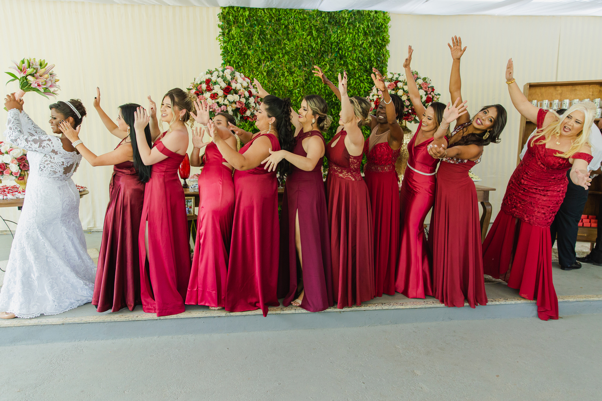 Madrinhas de vestido vermelho tentando pegar o buque que a noiva esta jogando durante festa de casamento animada ao ar livre em Itaocara no Rio de Janeiro.