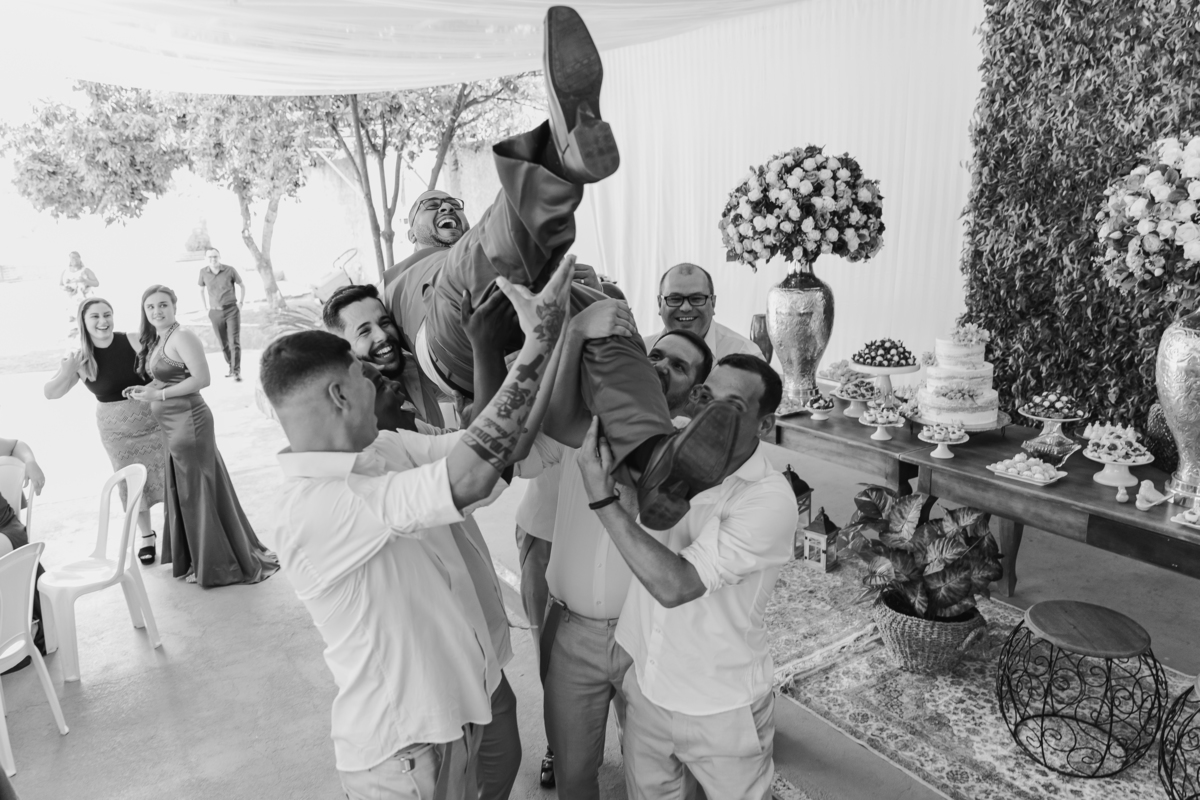 Padrinhos jogando o noivo para o alto em foto preta e branca durante festa animada de casamento em Itaocara no Rio de Janeiro.