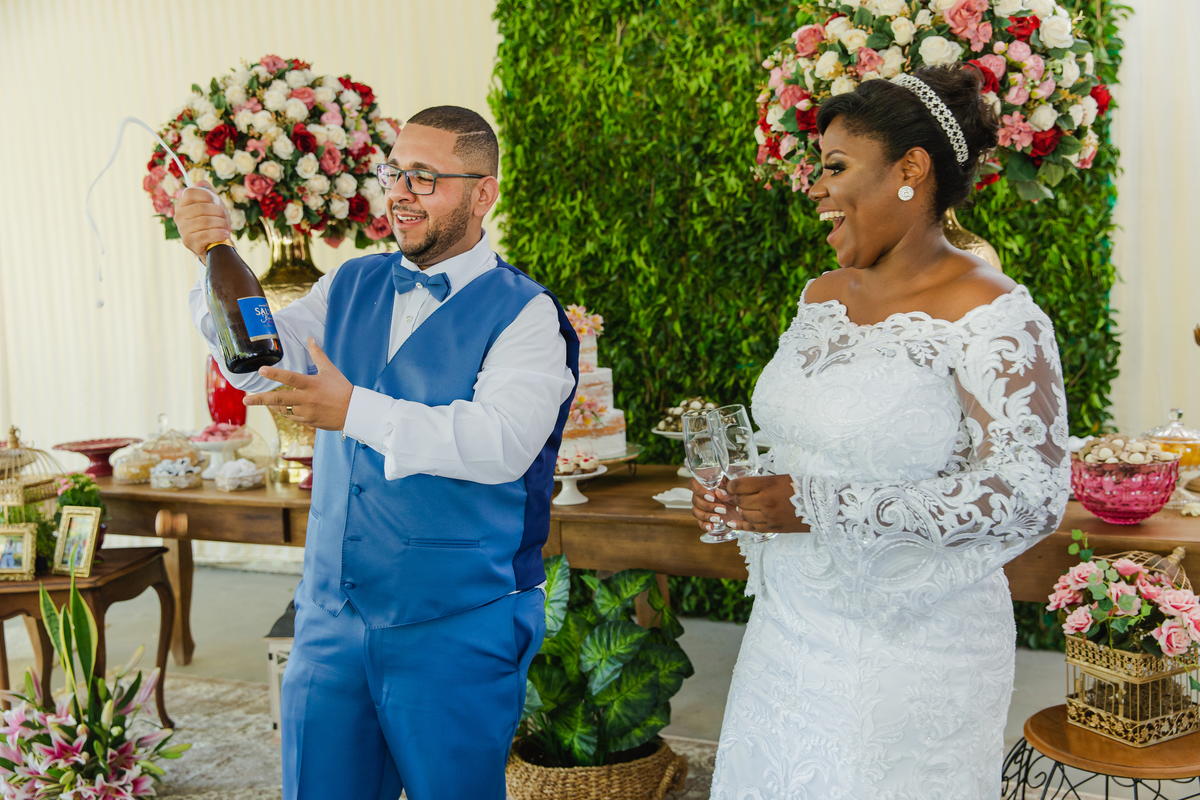 Noivo abrindo champanhe e noiva segurando as taças durantes festa linda de casamento ao ar livre em Itaocara no Rio de Janeiro. 