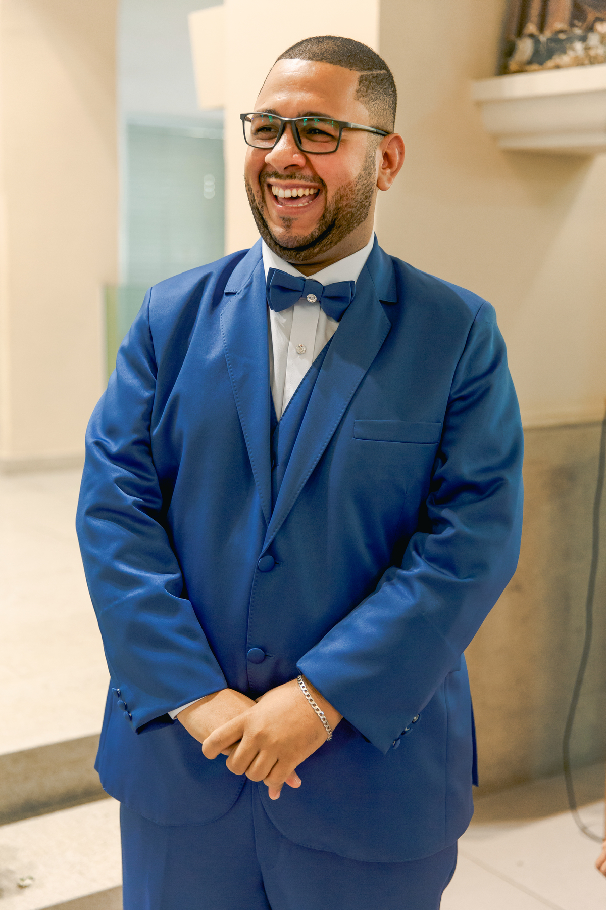 Noivo de terno azul e gravata borboleta dentro da igreja sorrindo aguardando a noiva entrar na igreja em casamento na igreja Paróquia de São José de Leonissa em Itaocara no Rio de Janeiro