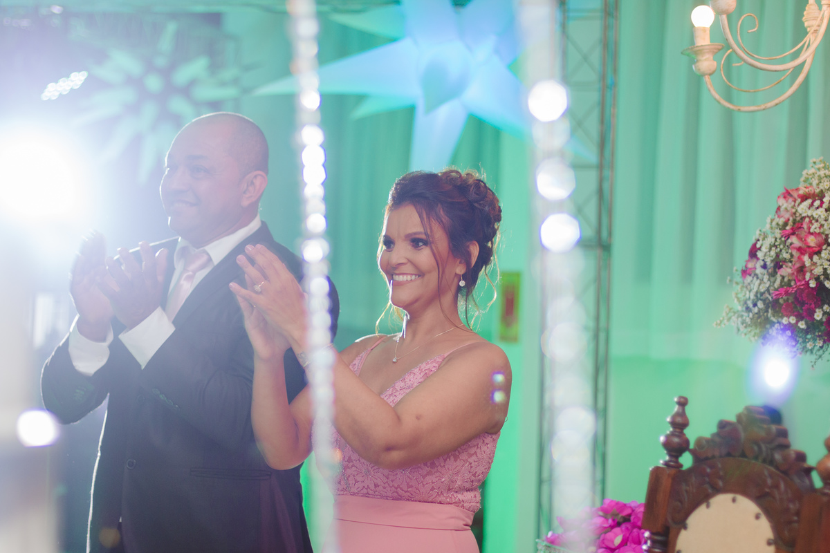 Pais felizes aplaudindo a filha durante festa de 15 anos em Santo Antônio de Pádua no Rio de Janeiro. Mãe da aniversariante vestindo vestido longo rosa.