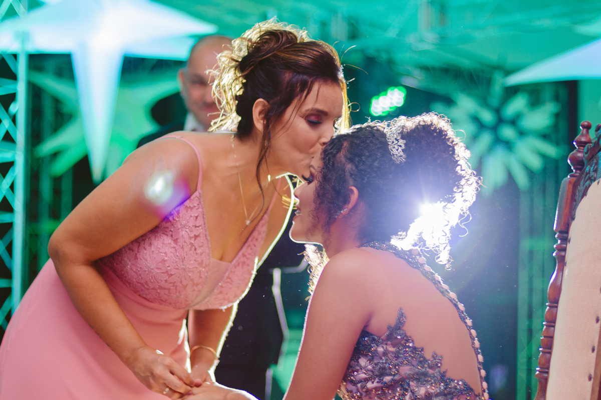 Mãe de aniversariante de 15 anos beijando a testa de sua filha e lhe dando um anel de presente durante festa de 15 anos em Santo Antônio de Pádua no RJ.