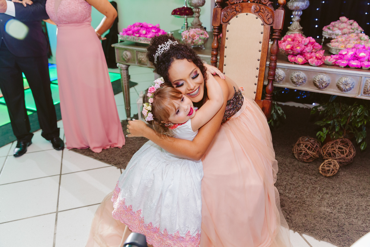 Debutante de 15 anos abraçando dama de honra com vestido rosa e sorrindo feliz durante sua festa de 15 anos em Santo Antônio de Pádua.