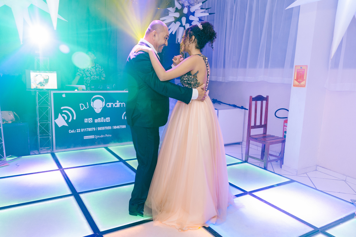Debutante linda de 15 anos com vestido longo com saia rosa dançando com seu pai a valsa na pista de dança com DJ Andinho durante festa de 15 anos em Pádua no RJ.
