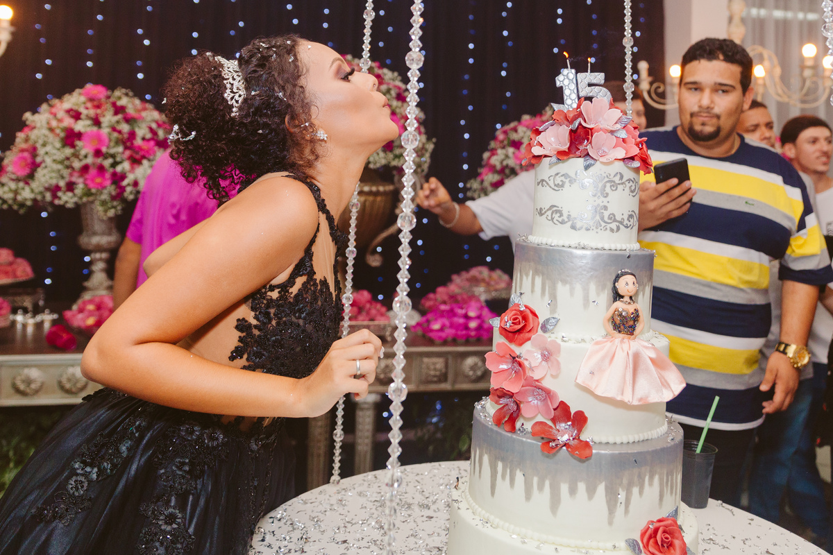 Aniversariante de 15 anos de vestido preto lindo assoprando a vela de seu bolo de aniversário durante festa de 15 anos em Santo Antônio de Pádua no Rio de Janeiro.