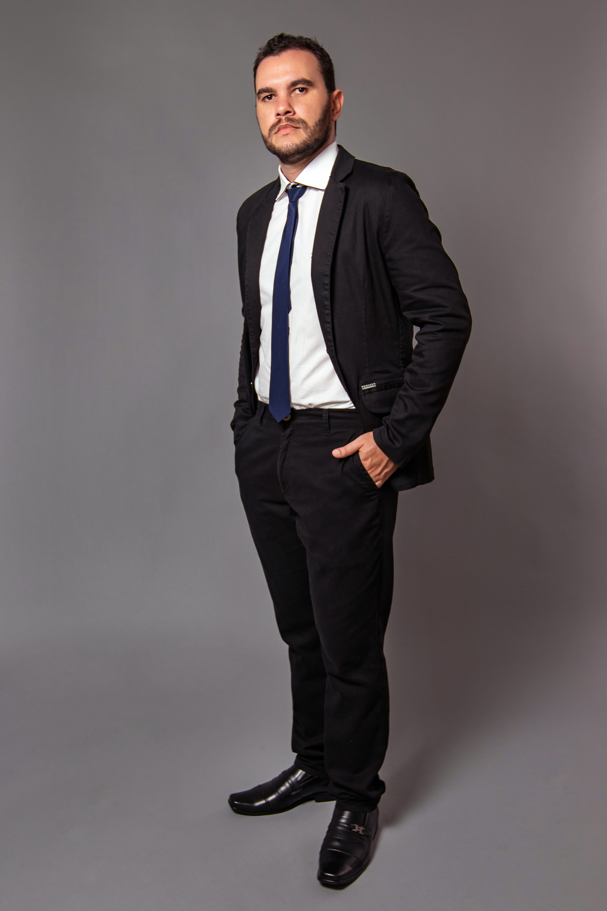 João Vitor em seu seu ensaio masculino em estúdio com terno e gravata preta no fundo fotográfico cinza em Santo Antonio de Pádua RJ