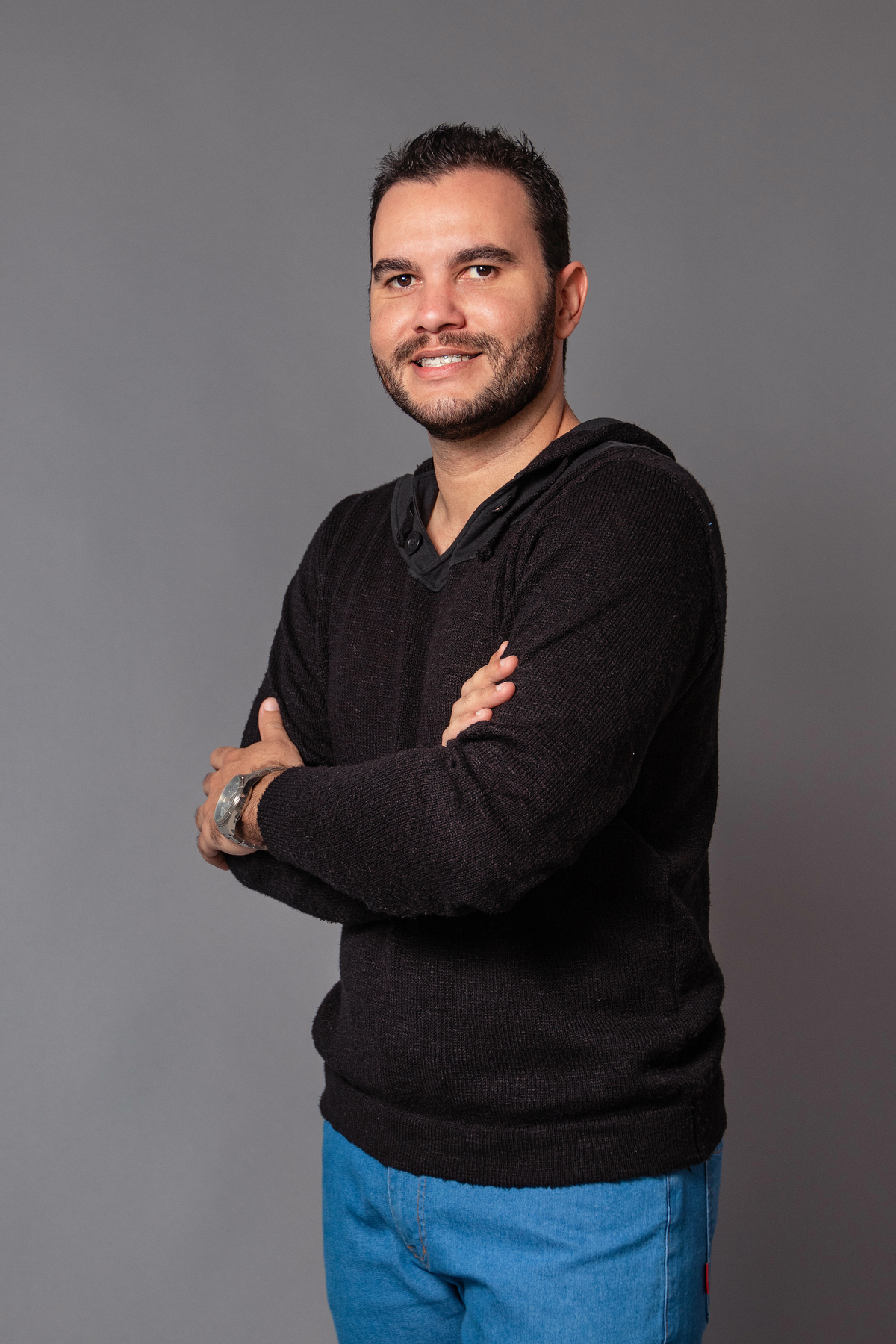 João Vitor em seu seu ensaio masculino com calça jeans e camisa preta fazendo pose em studio fotográfico com fundo fotográfico na cor cinza em Santo Antônio de Pádua no Rio de Janeiro 