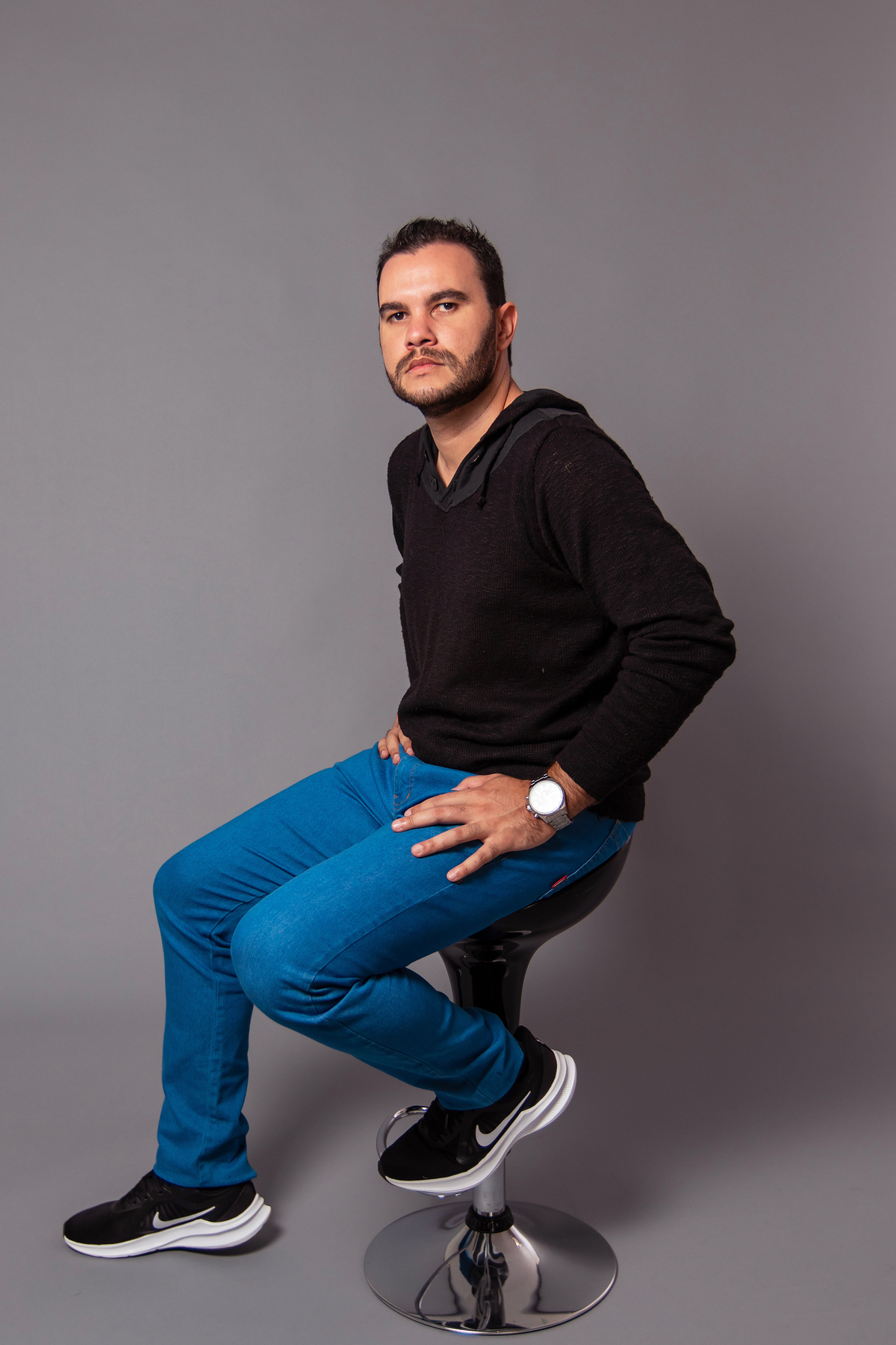 João Vitor em seu seu ensaio masculino com calça jeans e camisa preta fazendo pose em studio fotográfico com fundo fotográfico na cor cinza em Santo Antônio de Pádua no Rio de Janeiro 