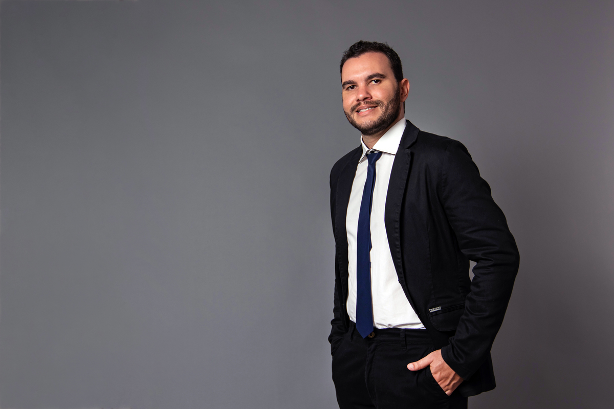 João Vitor em seu seu ensaio masculino em estúdio com terno e gravata preta no fundo fotográfico cinza em Santo Antonio de Pádua RJ