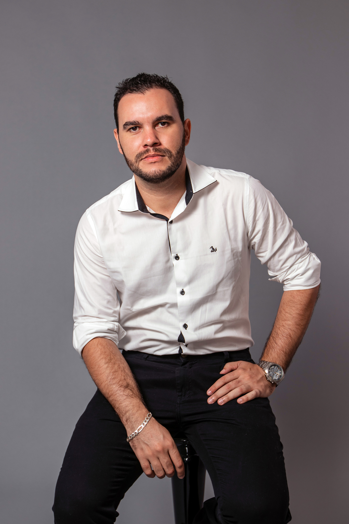 João Vitor em seu seu ensaio masculino em estúdio com camisa branca e calça social preta no fundo fotográfico cinza em Santo Antonio de Pádua no interior do RJ