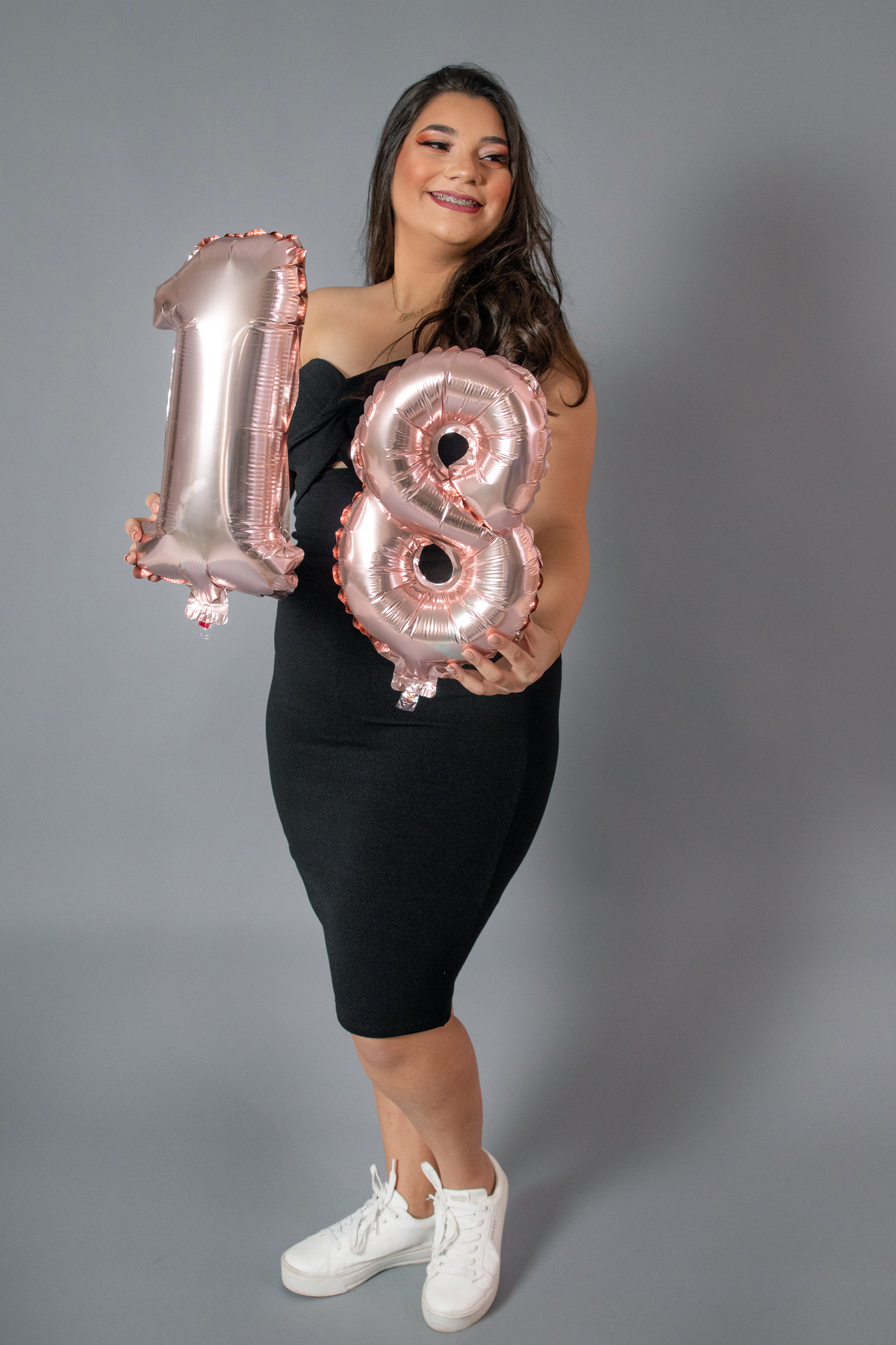 Ensaio feminino de 18 anos, com vestido preto, make perfeita em fundo cinza, e balões com números em 18 em estúdio em Santo Antônio de Pádua no Rio de Janeiro.