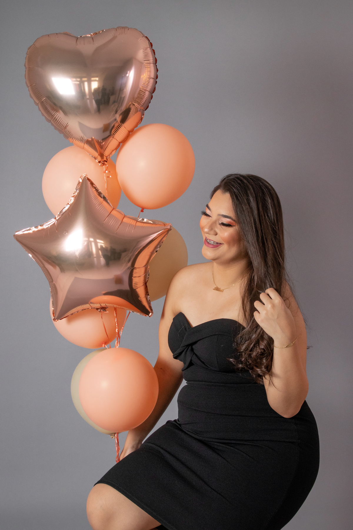 Ensaio feminino de 18 anos, com vestido preto, make perfeita em fundo cinza e balões na cor rosê e pessêgo em estúdio em Santo Antônio de Pádua no Rio de Janeiro.