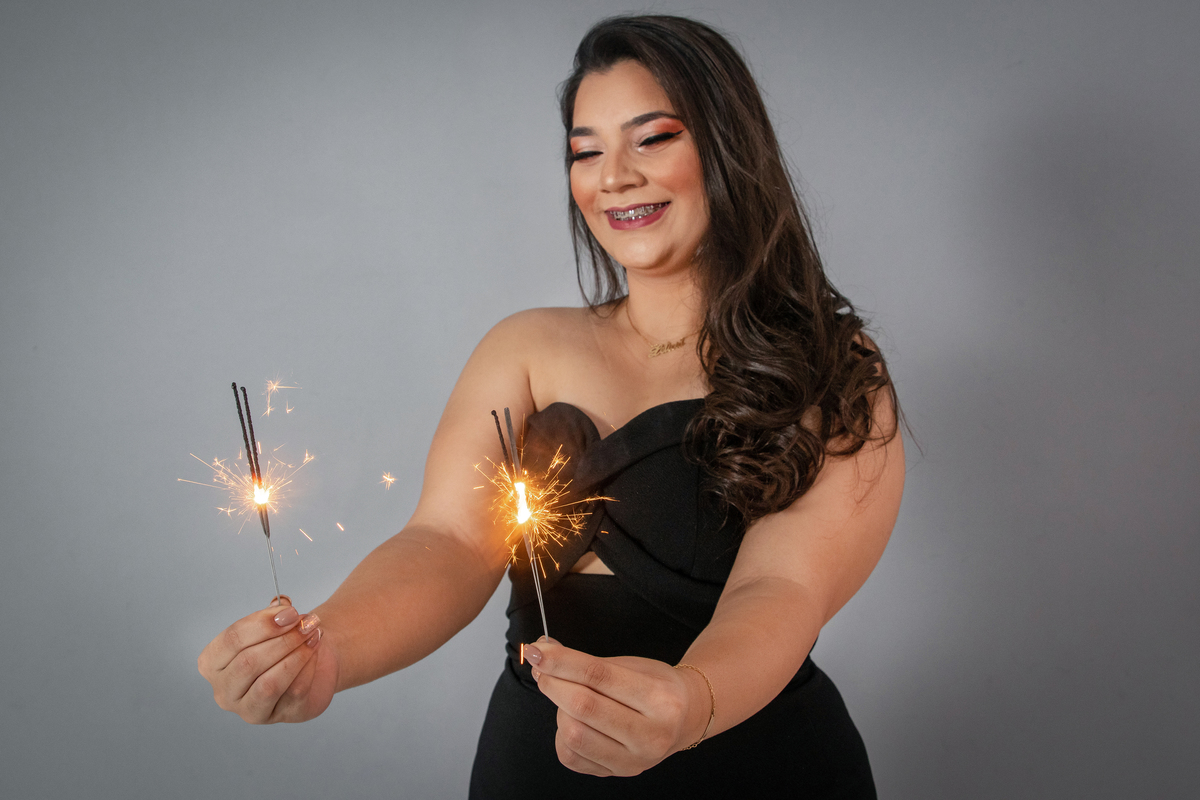 Ensaio feminino de 18 anos, com vestido preto, velas para comemorar, make perfeita em fundo cinza em estúdio em Santo Antônio de Pádua no Rio de Janeiro.
