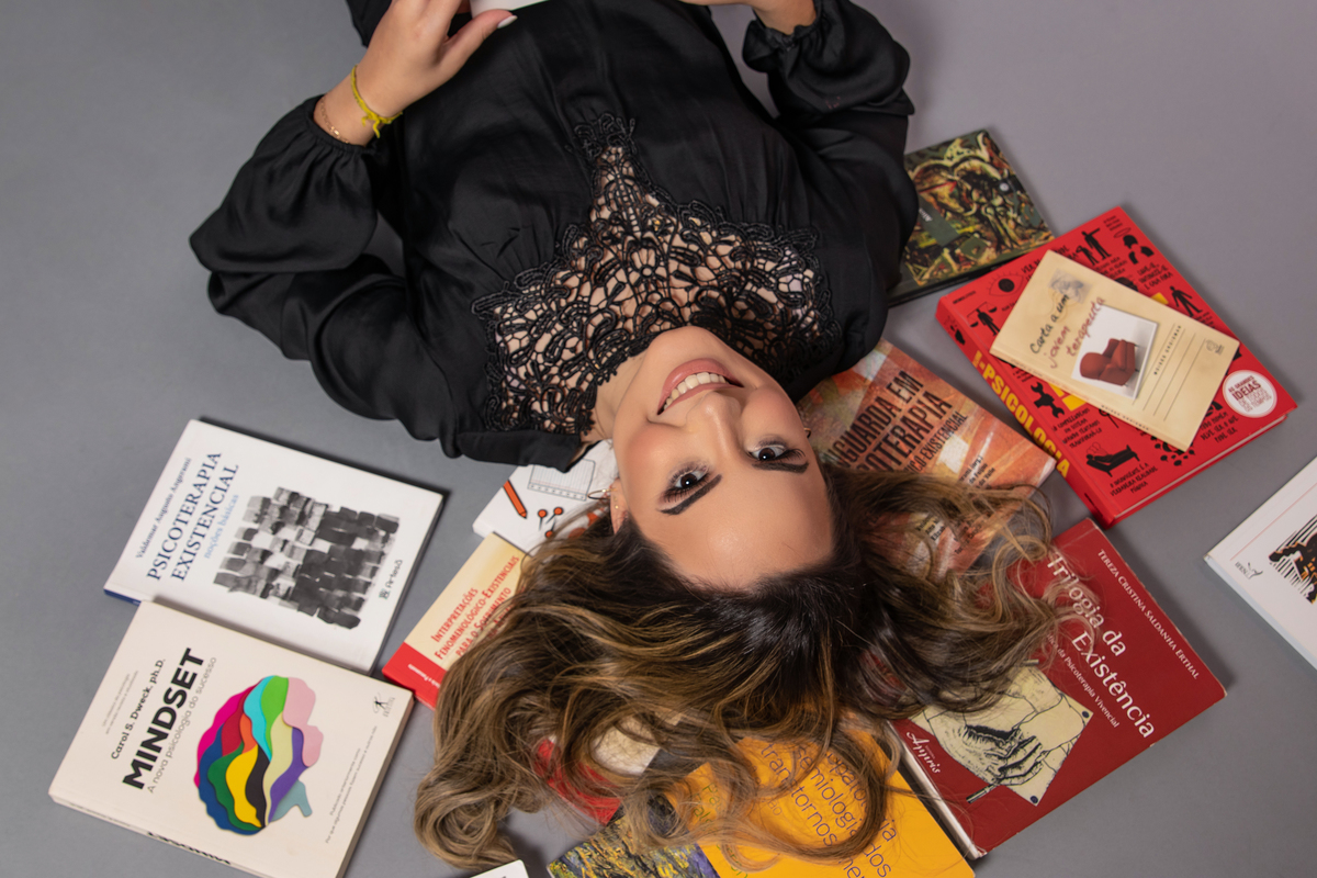 Ensaio em estúdio de formanda em psicologia deitada em cima dos livros com roupa preta e a maquiagem perfeita em Santo Antônio de Pádua no Rio de Janeiro.