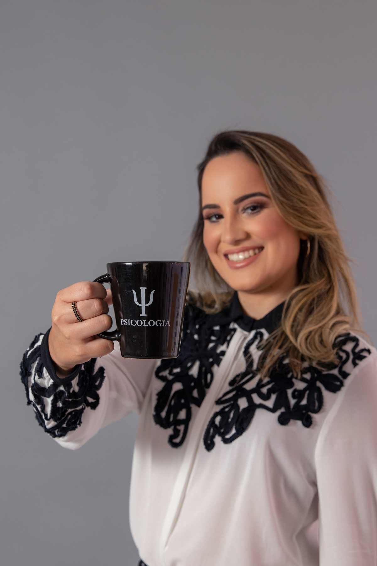 Formanda em psicologia em pé segurando uma caneca com uma camisa branca em ensaio realizado em estúdio em Pádua no Rio de Janeiro