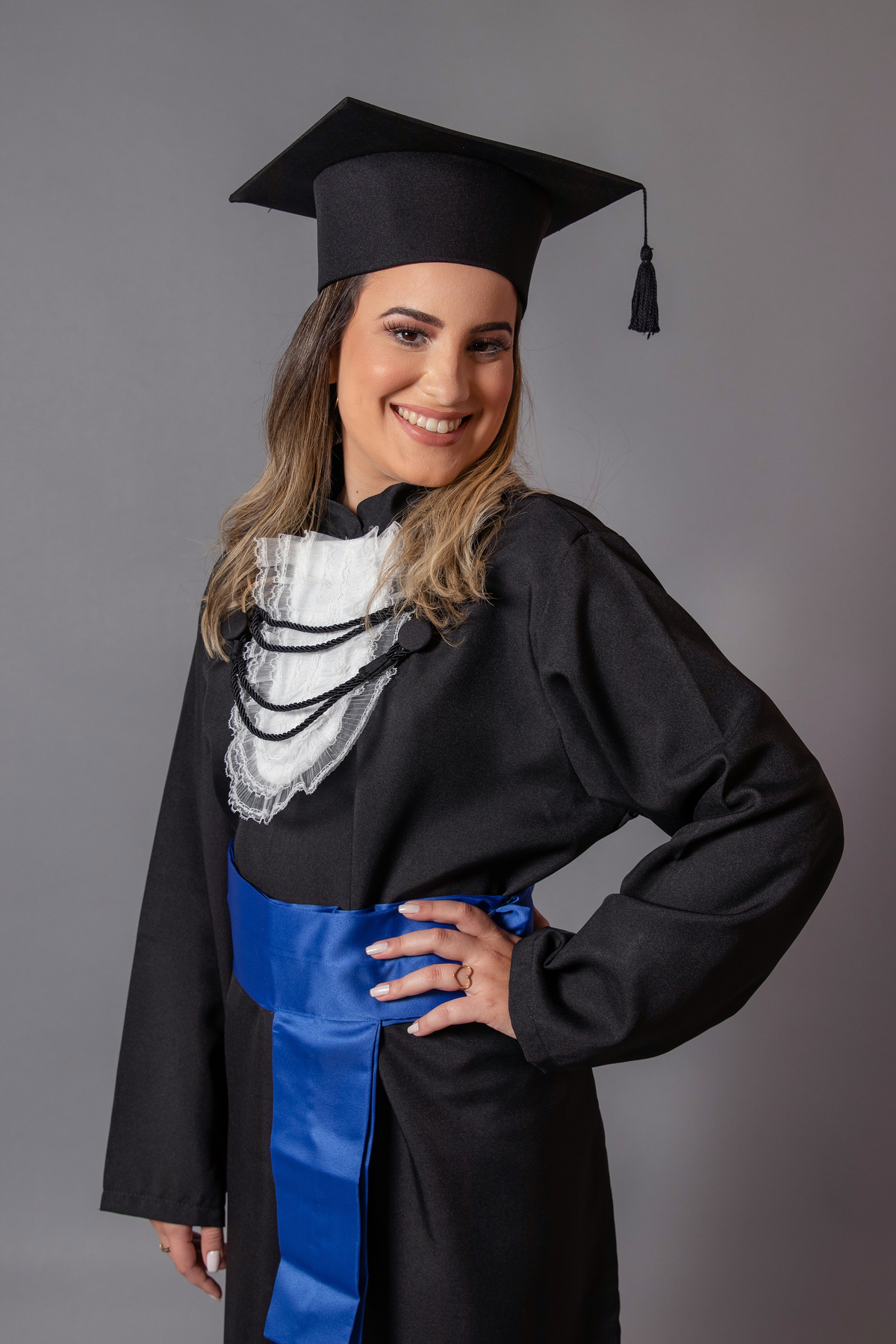 Formanda vestindo beca com faixa azul em seu ensaio de formanda em psicologia em estudio realizado em Santo Antônio de Pádua no RJ