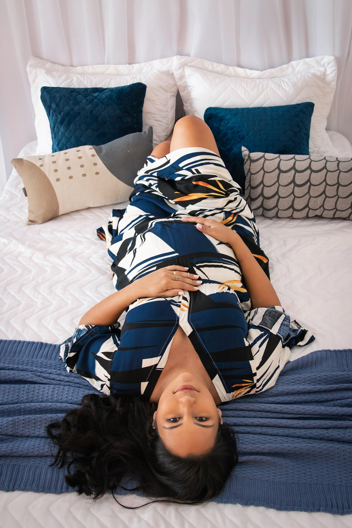 Grávida linda com vestido estampado azul longo deitada na cama em quarto lindo montado em estúdio em Santo Antônio de Pádua RJ.