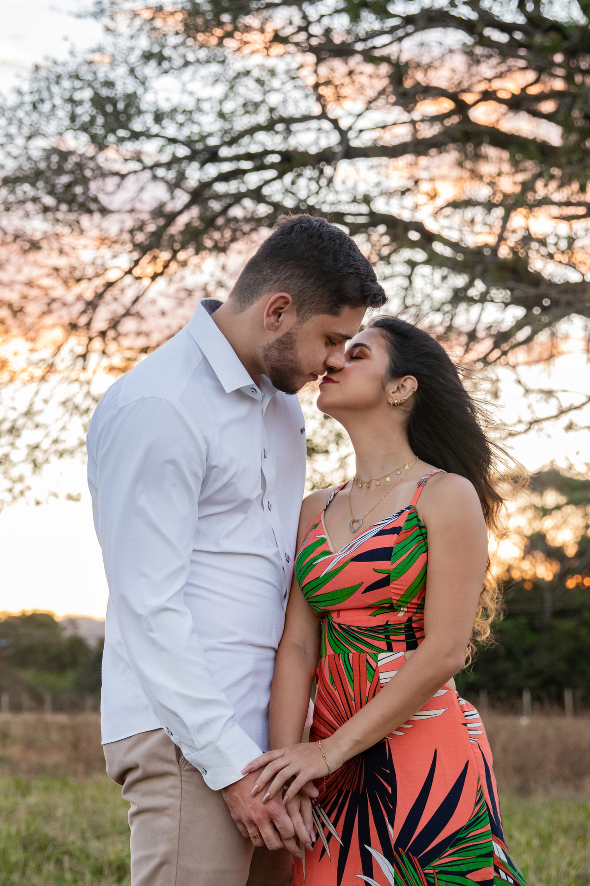  Casal se beijando em baixo de uma arvore enorme e linda em seu ensaio pre casamento. A noiva usa vestido laranja combinando como por do sol em Itaocara no interior do Rio de Janeiro.