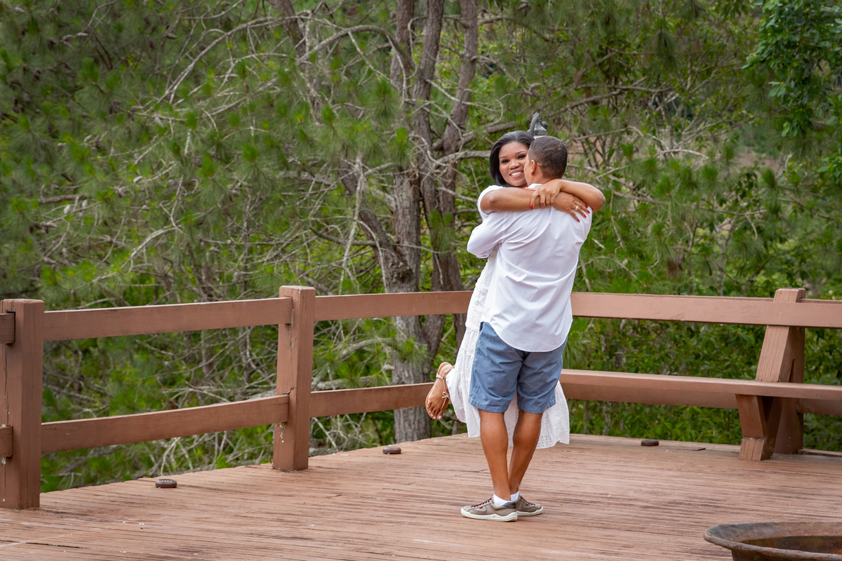 Ensaio pré casamento nublado na serra de Teresópolis, noiva e noivo com roupas brancas abraçados no deque de uma casa linda com muito verde e muitas flores e hortênsias azuis em Pàdua RJ.