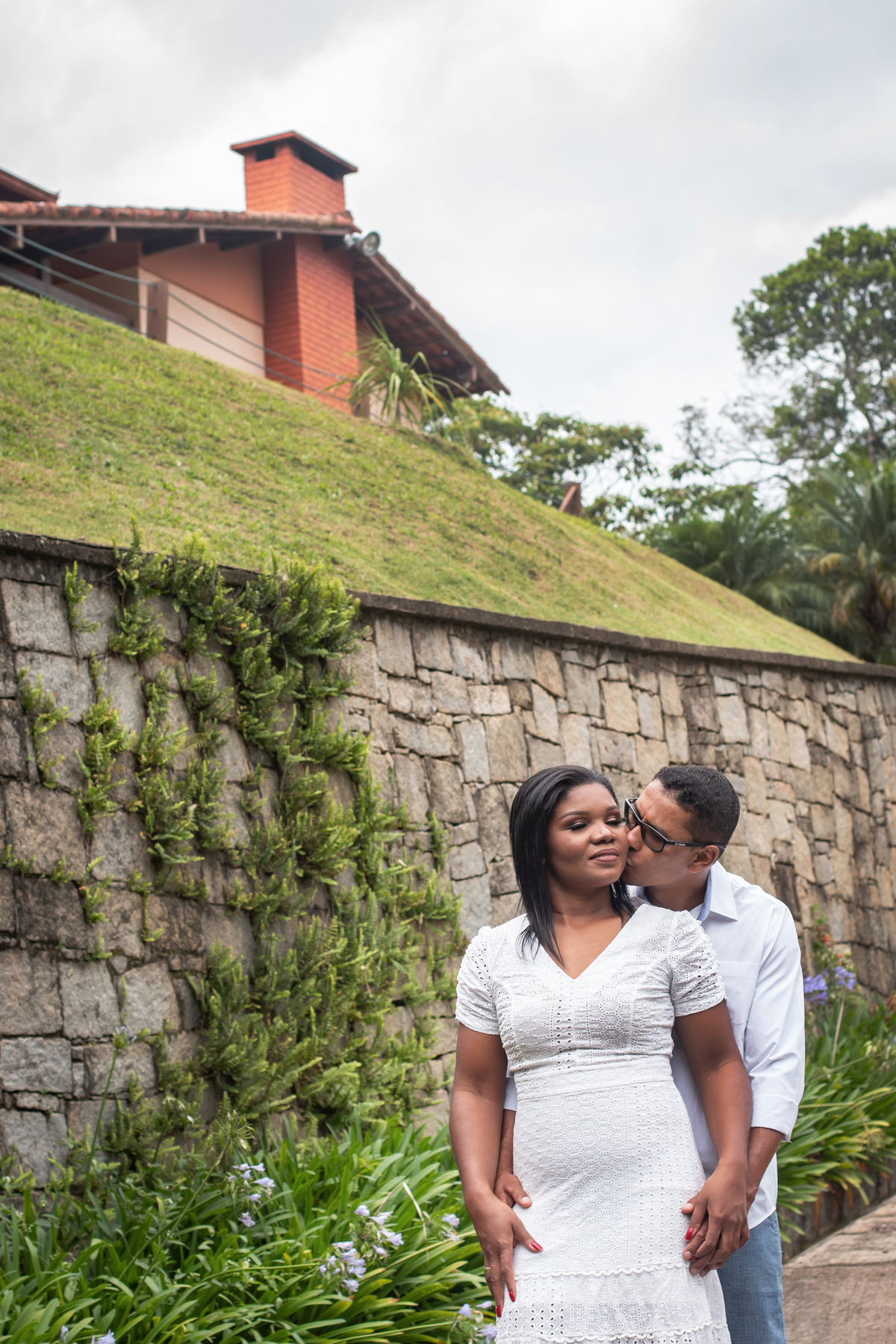 Noivo beijando a noiva em ensaio pré casamento na serra de Teresópolis, noiva e noivo com roupas brancas em uma casa linda com muito verde e muitas flores e hortênsias azuis em Pàdua RJ.