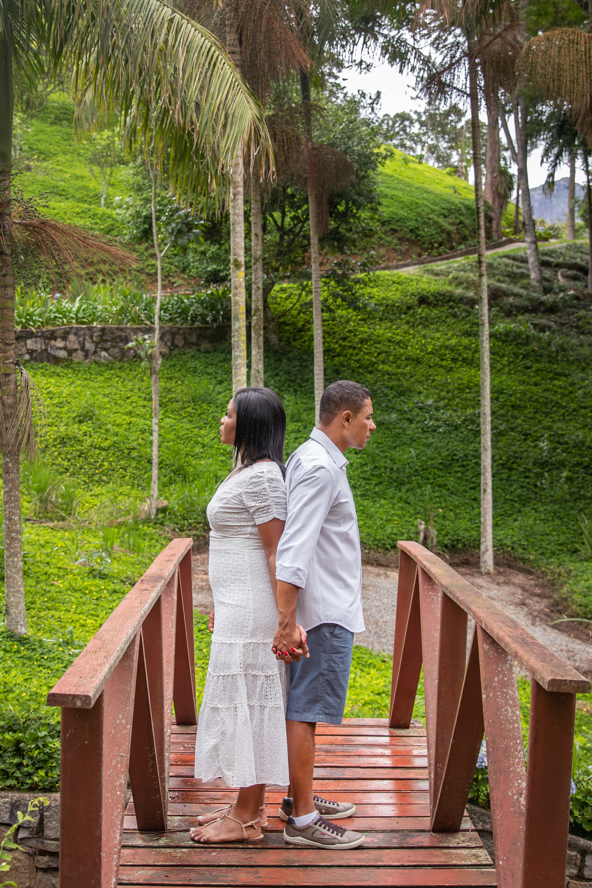 Noivos um de costas para o outro em ensaio pré wedding em dia nublado na serra de Teresópolis, noiva e noivo com roupas brancas em uma casa linda com muito verde e muitas flores e hortênsias azuis em Pàdua RJ.