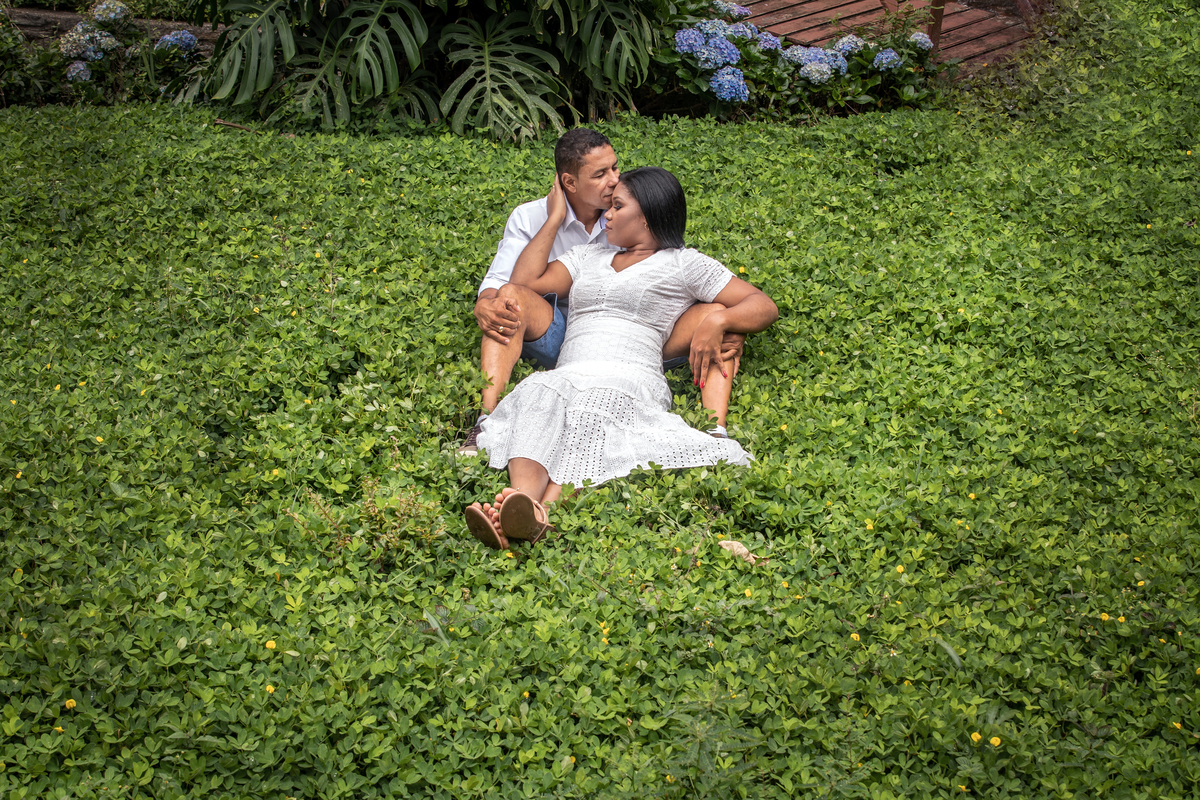 Noivos sentados no meio da grama o na serra de Teresópolis, noiva e noivo com roupas brancas em uma casa linda com muito verde e muitas flores e hortênsias azuis em seu ensaio pré casamento 
RJ.