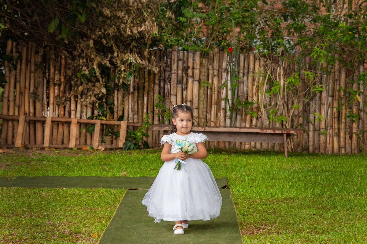 Dama de honra com boque com flores azuis entrando na cerimônia ao ar livre durante casamento em Pádua interior do Rio de Janeiro.