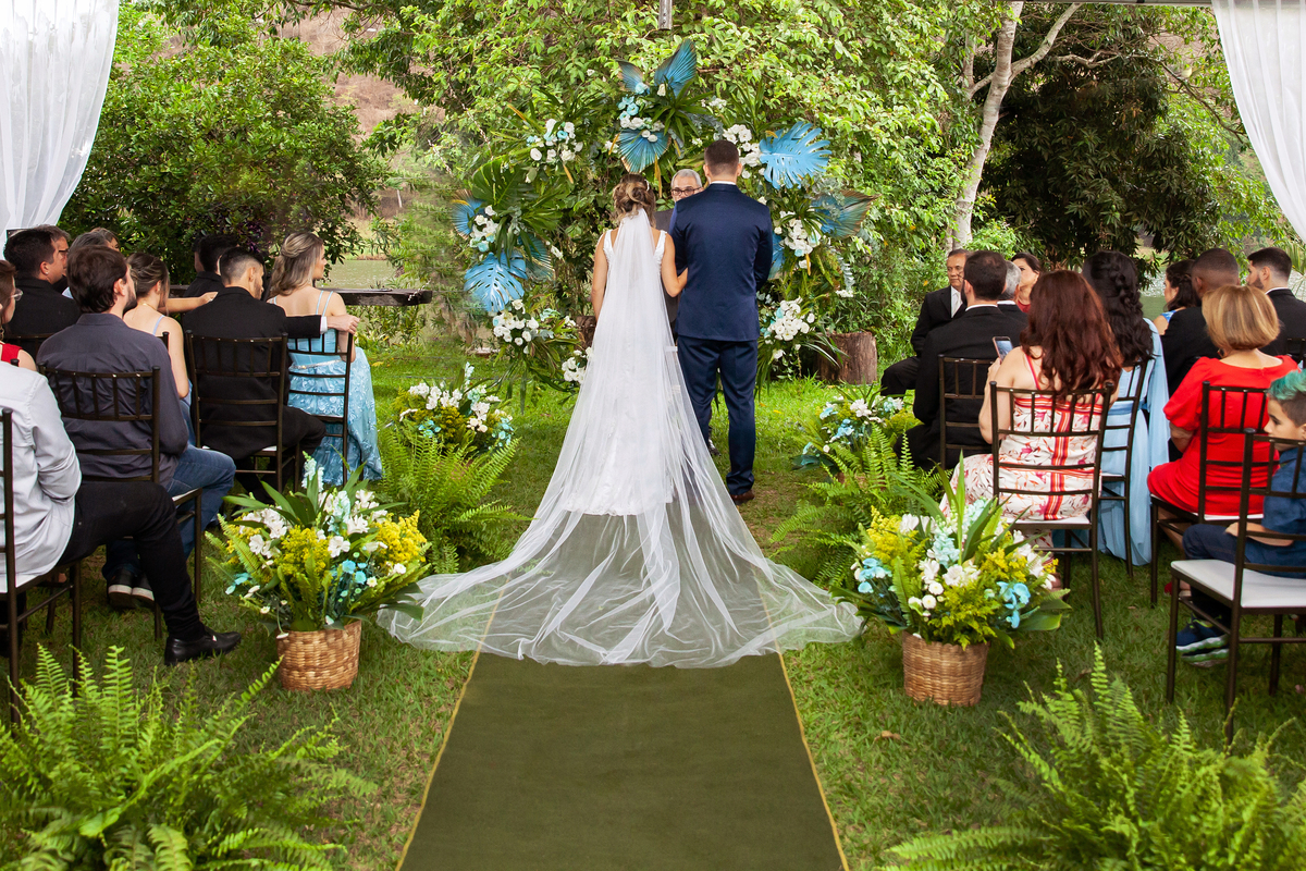 Vestido da noiva todo justo com um enorme véu e terno do noivo azul durante casamento ao ar livre em Pádua interior do Rio de Janeiro.