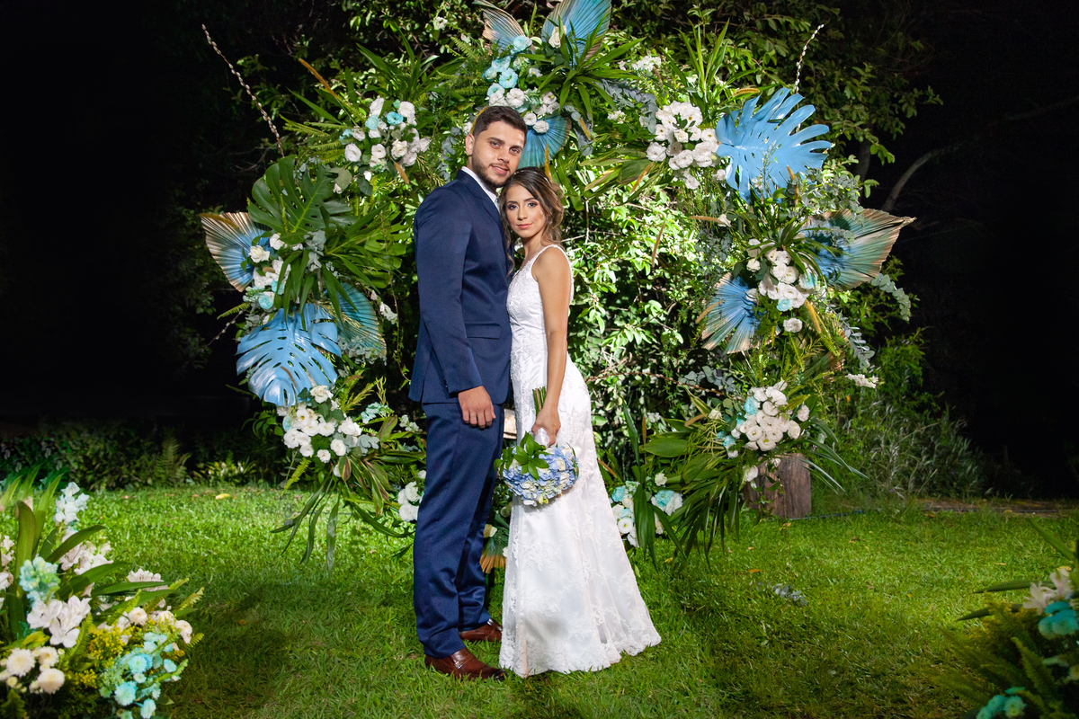 Noivos lindos e felizes em um arco de flores azuis e costela de adão em durante festa de casamento ao ar livre em Pádua  interior do Rio de Janeiro.