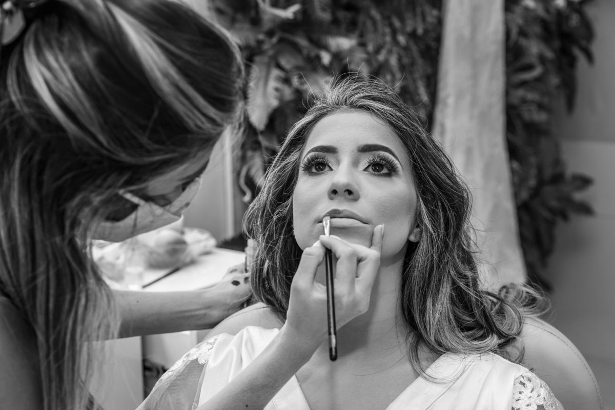 Noiva em foto preta e branca sendo maquiada durante seu making off minutos antes do seu casamento no salão da Thais Dalet em Santo Antônio de Pádua - RJ.