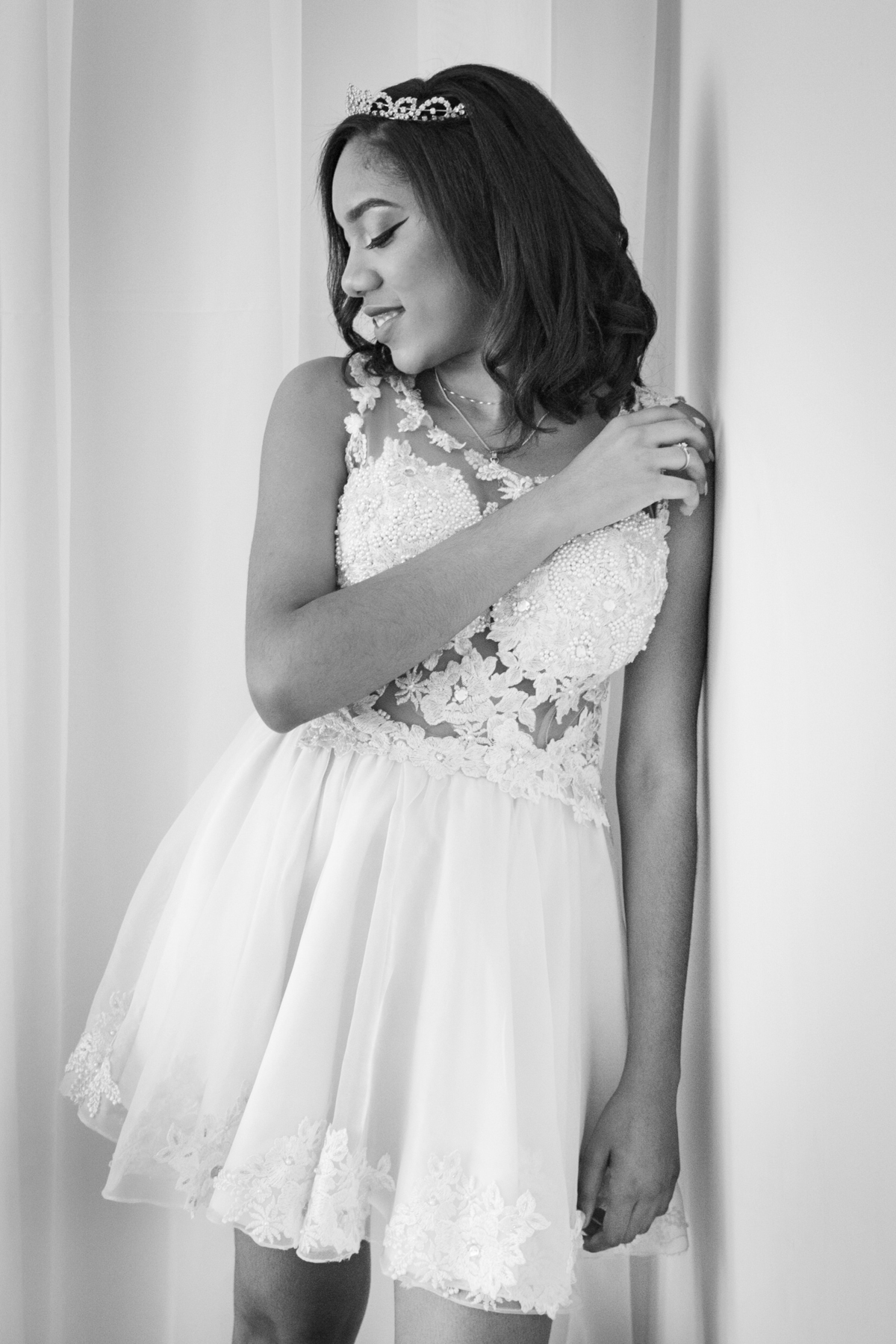 Debutante de 15 anos com vestido amarelo de renda fazendo seu ensaio em estúdio, encostada na parede e com a mão por cima da cabeça  em Santo Antônio de Pádua no interior do Rio de Janeiro. Foto preta e branca.