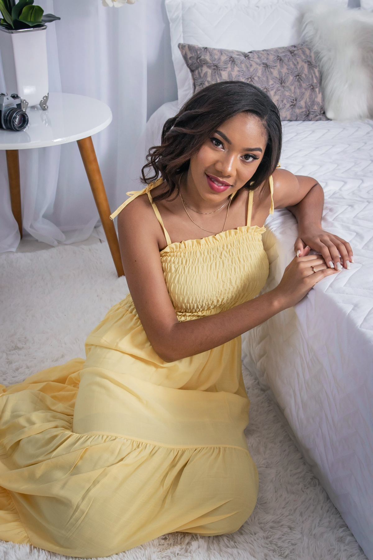 Ensaio 15 anos em estúdio, debutante com vestido amarelo encostada na cama sorrindo com a mão no queixo em Santo Antônio de Pádua no interior do Rio de Janeiro.