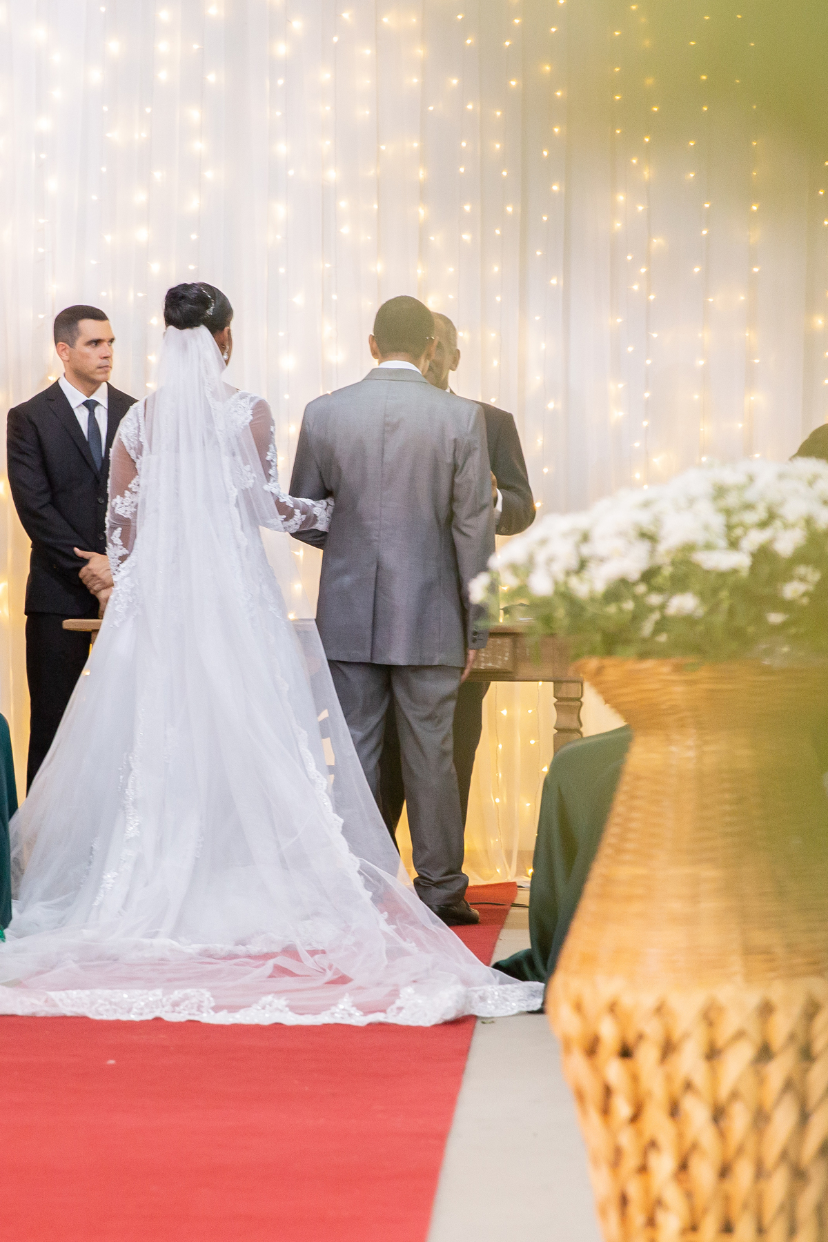 Noiva com vestido de renda e véu lindo e noivo com terno cinza de costas durante cerimônia evangélica casamento durante a noite em um sitio em Cambuci no interior do Rio de Janeiro.