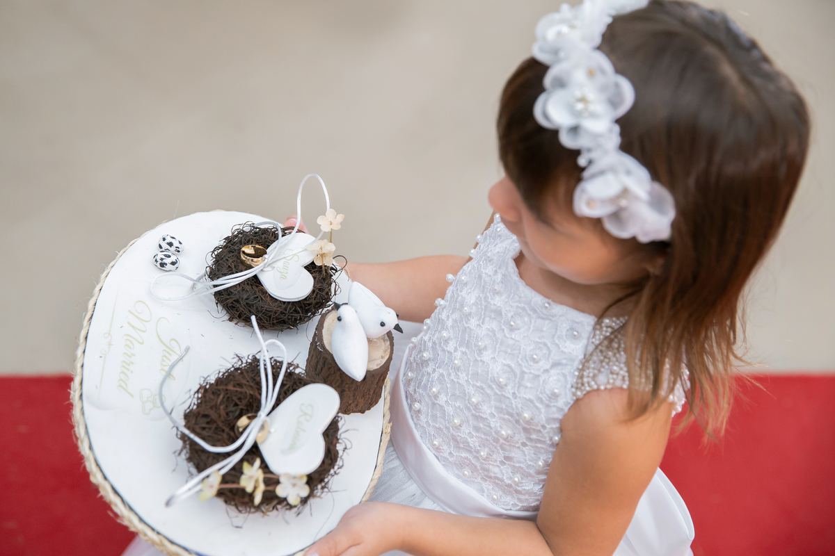 Dama entrando com as alianças em um lindo porta alianças feito de feltro com passaarinhos. Dama linda e sorrindo durante cerimônia evangélica em um casamento a noite em um sitio em Cambuci no interior do Rio de Janeiro.