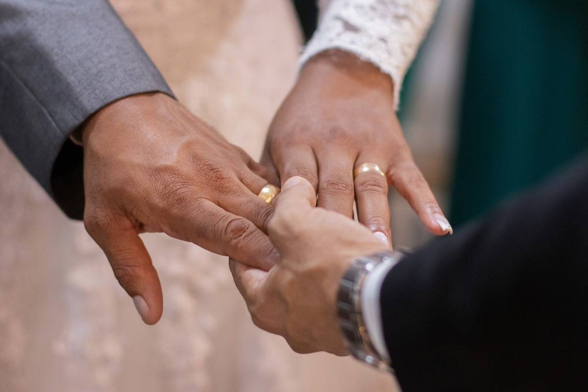 Detalhes das mãos das alianças dos noivos durante oração em uma cerimônia linda evangélica em um casamento a noite em um sitio em Cambuci no interior do Rio de Janeiro.