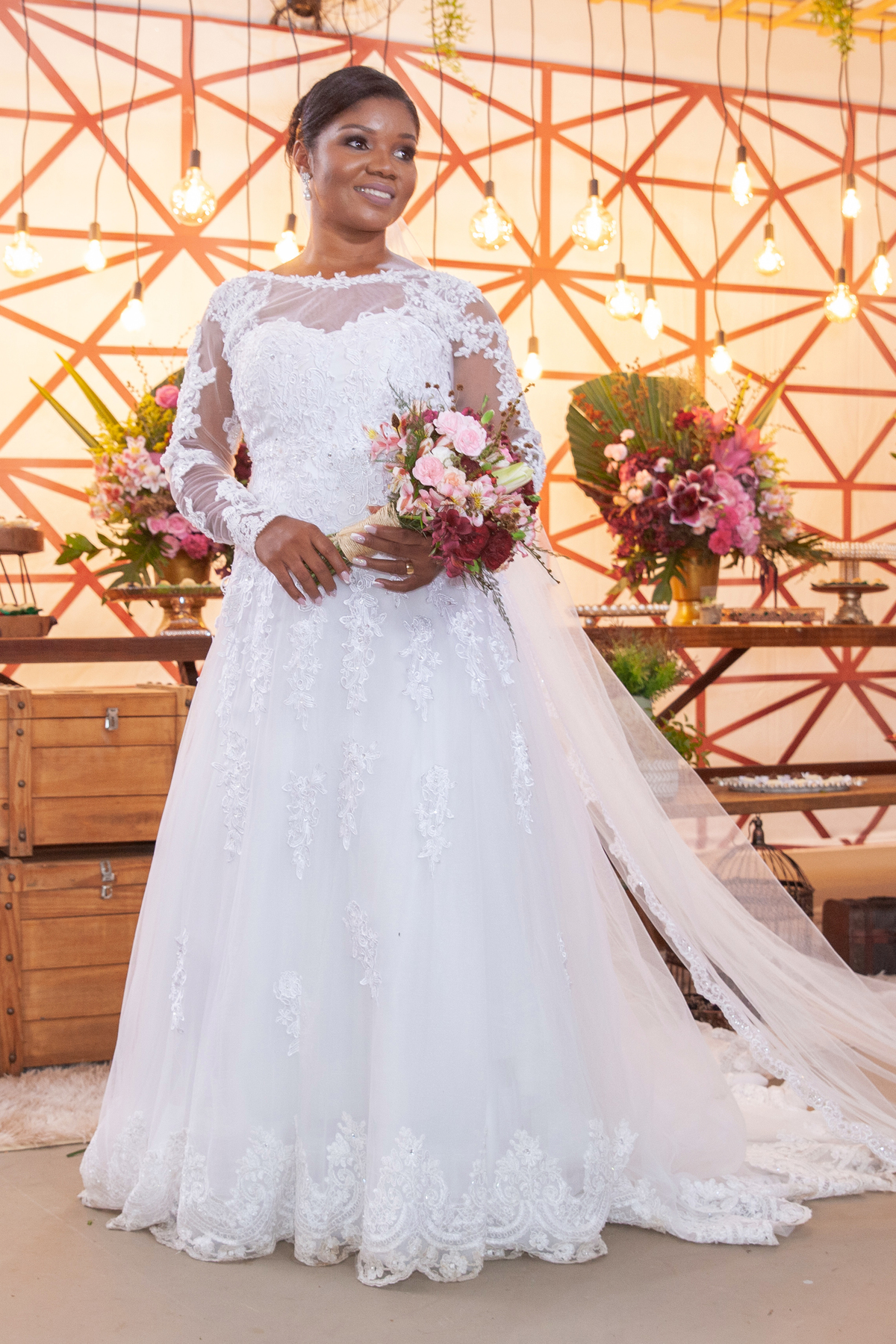 Noiva com vestido de renda e véu lindo fazendo fotos com seu buquê com flores em tons de vermelho durante cerimônia evangélica em casamento durante a noite em um sitio em Cambuci no interior do Rio de Janeiro.