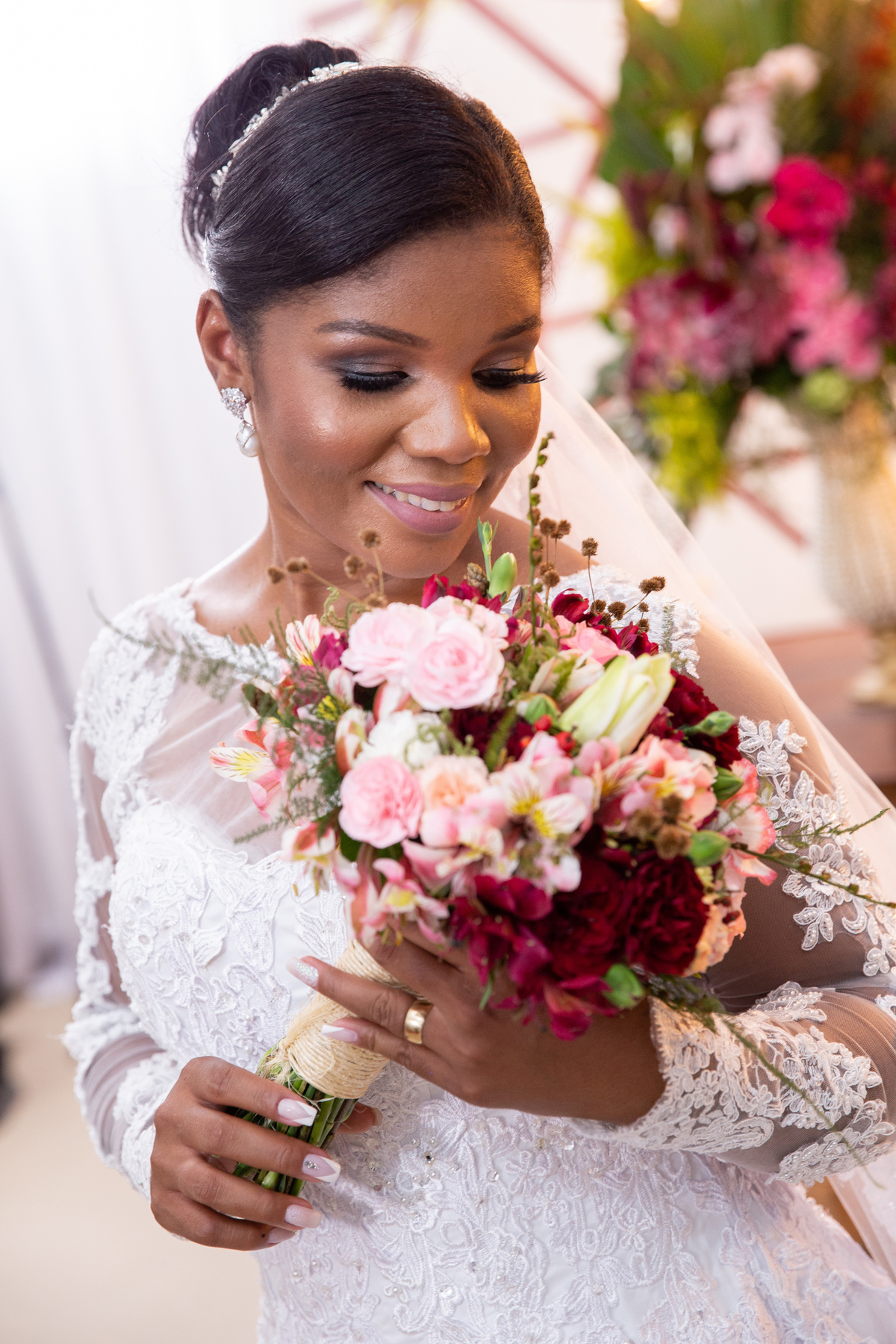 Noiva com vestido de renda e véu lindo fazendo fotos com seu buquê com flores em tons de vermelho durante cerimônia evangélica em casamento durante a noite em um sitio em Cambuci no interior do Rio de Janeiro.