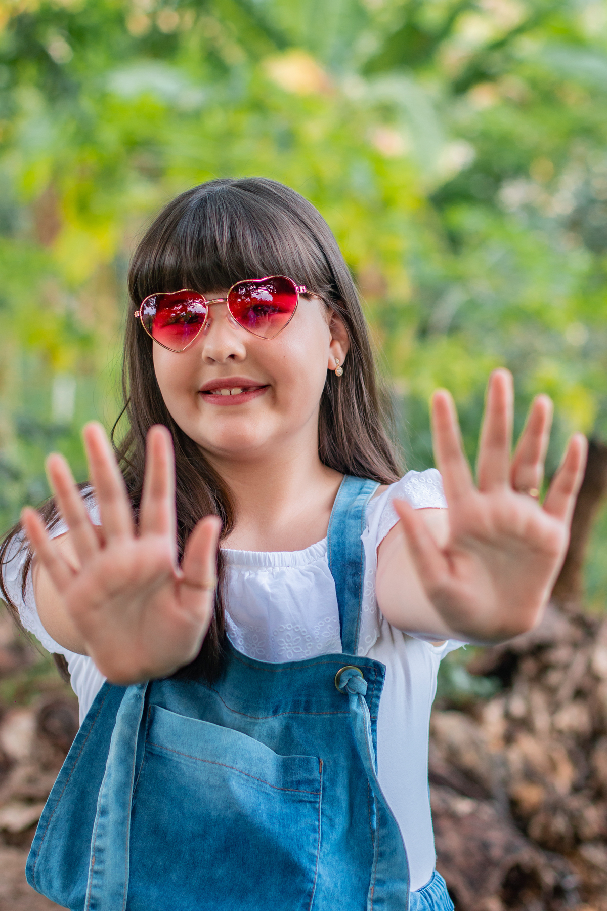 Ensaio de fotos ao ar livre com muito verde, menina com macacão jeans linda, toda feliz comemorando seu aniversário de 10 anos com óculos decoração estúdio em Santo Antônio de Pádua no Rio de Janeiro.
