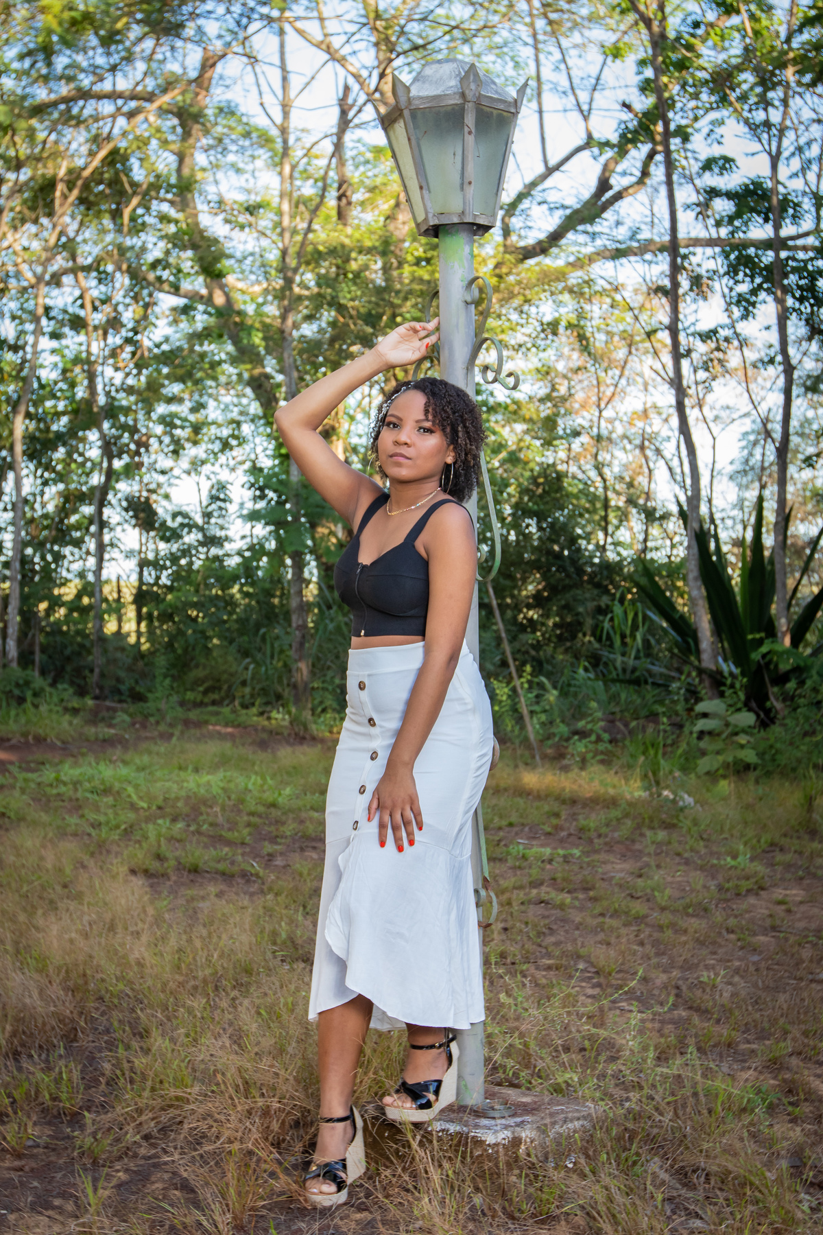 Aniversariante linda de 15 anos, com cabelo cacheado em um dia lindo com muito verde ao por do sol parque municipal de Miracema em seu ensaio de 15 Anos. No interior do Rio de Janeiro.