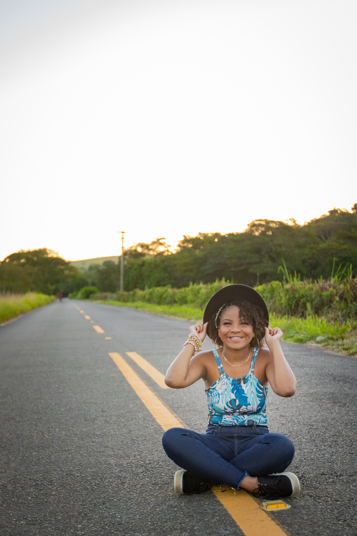 Aniversariante linda de 15 anos, com cabelo cacheado em um dia lindo com muito verde ao por do sol lindo no meio do asfalto em seu ensaio de 15 Anos. No interior do Rio de Janeiro.