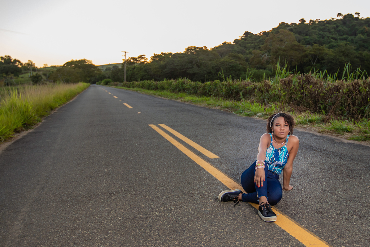 Aniversariante linda de 15 anos, com cabelo cacheado em um dia lindo com muito verde ao por do sol lindo no meio do asfalto em seu ensaio de 15 Anos. No interior do Rio de Janeiro.