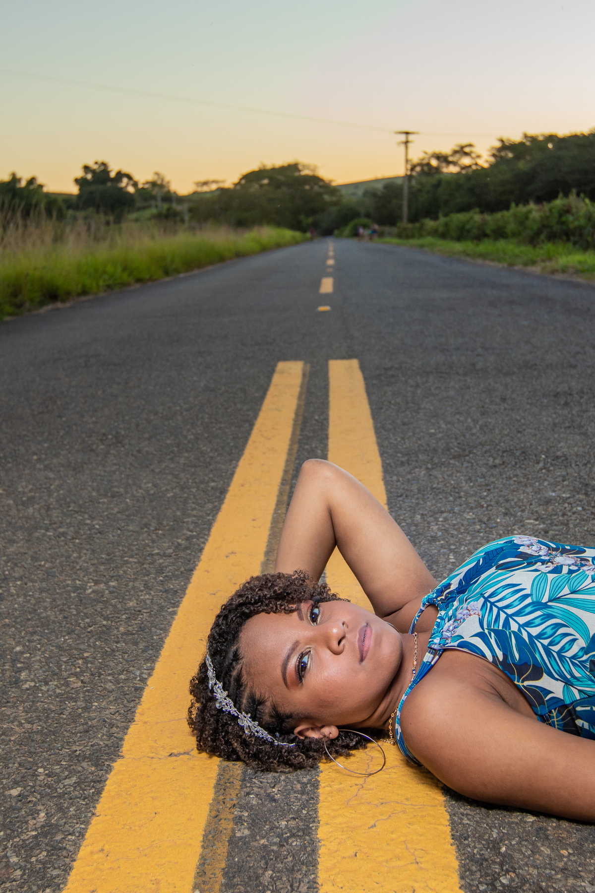 Aniversariante linda de 15 anos, com cabelo cacheado em um dia lindo com muito verde ao por do sol lindo no meio do asfalto em seu ensaio de 15 Anos. No interior do Rio de Janeiro.