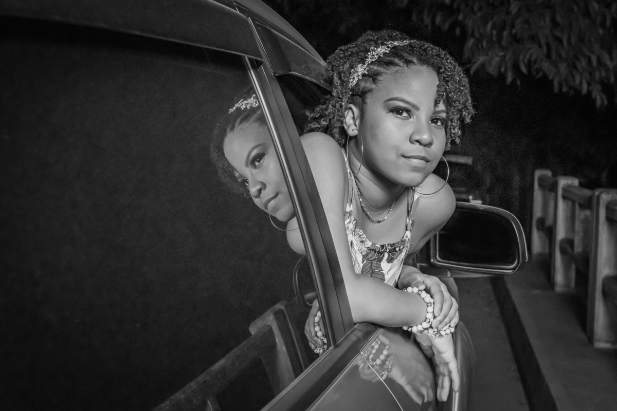 Aniversariante linda de 15 anos, com cabelo cacheado em um dia lindo com muito verde ao por do sol lindo no meio do asfalto em seu ensaio de 15 Anos. No interior do Rio de Janeiro. Foto preta e branca.