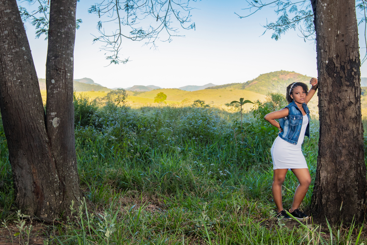 Aniversariante linda com jaqueta jeans em um campo florido com um céu azul perfeito no parque municipal de Miracema em seu ensaio de 15 Anos. No interior do Rio de Janeiro.